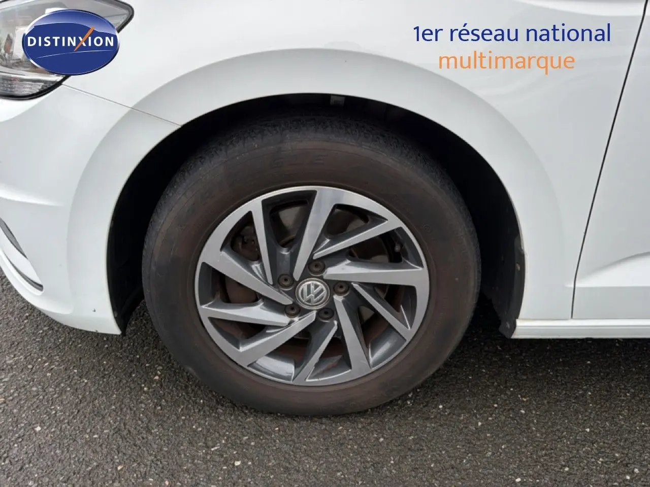 Gros plan sur la roue avant gauche d’un Volkswagen Touran blanc avec jante alliage gris foncé.