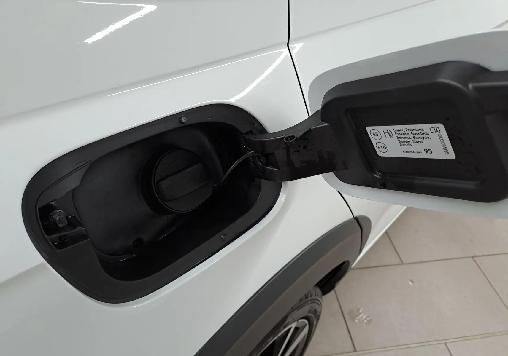 Gros plan sur la trappe à carburant ouverte côté gauche d’un Volkswagen Taigo blanc pur toit noir, jantes 18 pouces visibles.