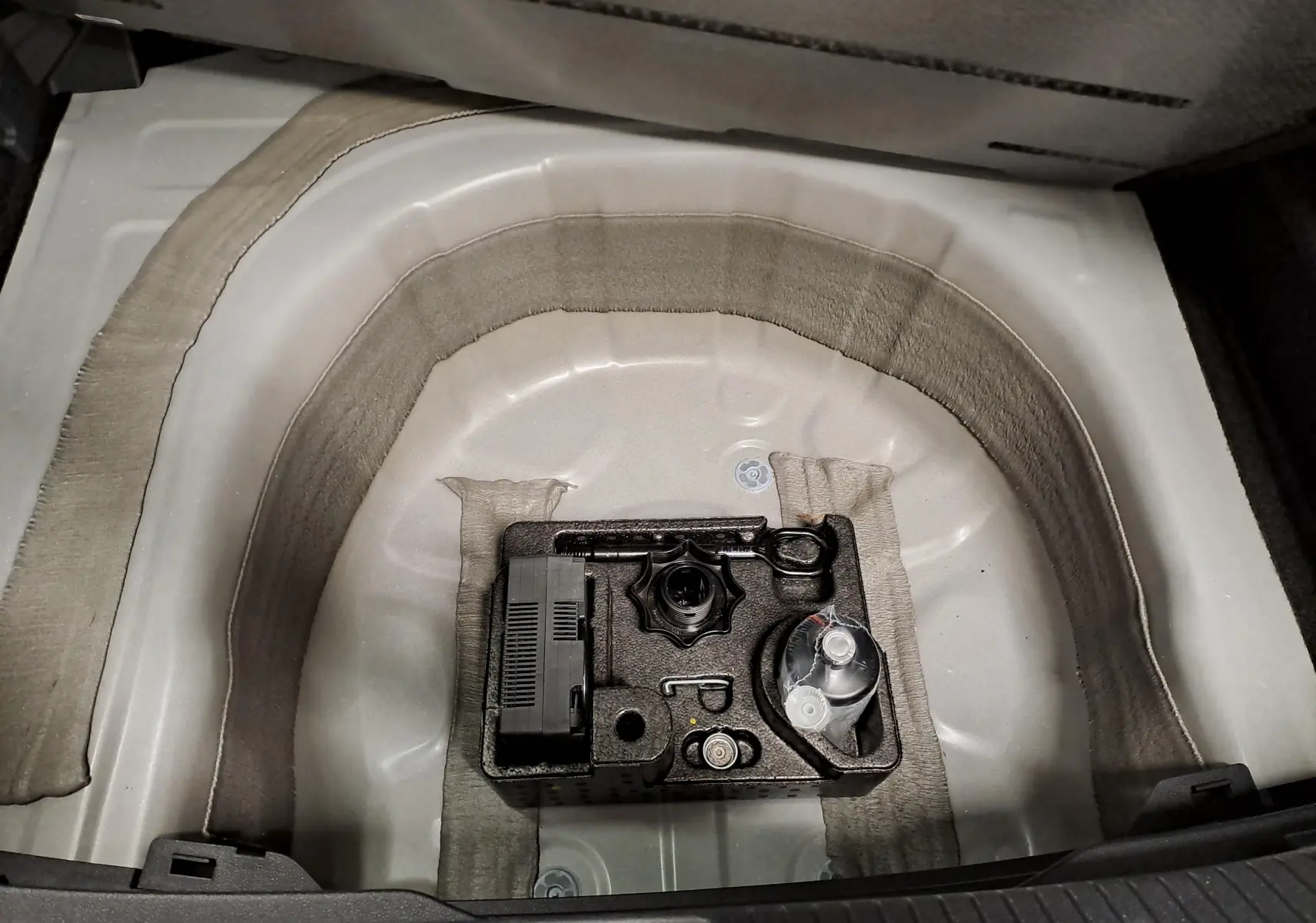 Vue du coffre ouvert du Volkswagen Taigo blanc pur toit noir, montrant le compartiment de rangement sous la moquette.