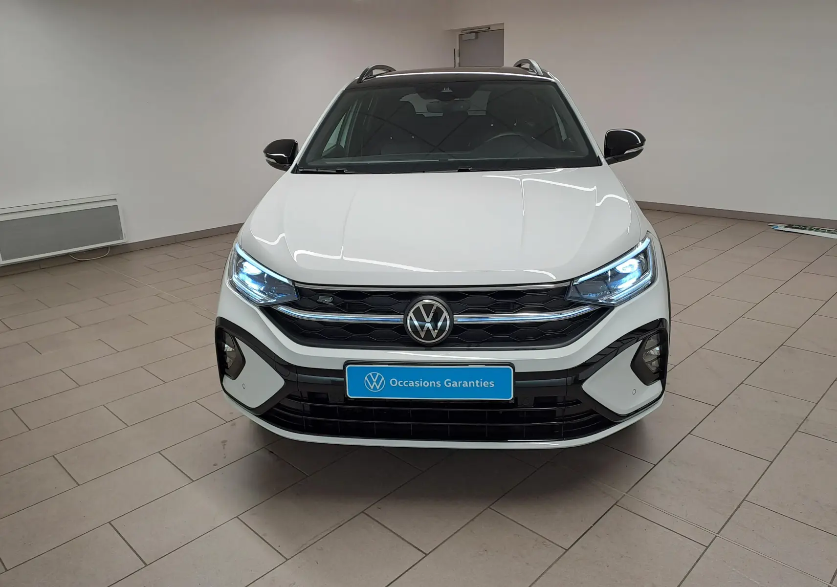 Vue frontale du Volkswagen Taigo 1.5 TSI 150 DSG7 R-Line Edition blanc pur avec toit noir et feux LED allumés.