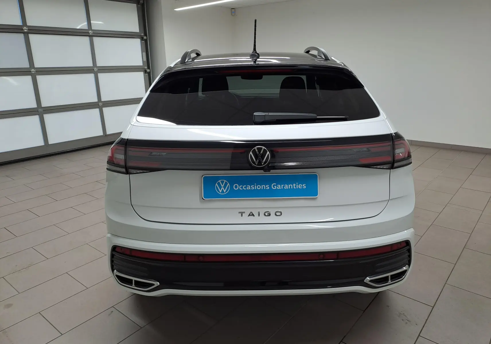 Vue arrière d'un Volkswagen Taigo blanc pur avec toit noir, feux arrière connectés et double sortie d'échappement chromée.