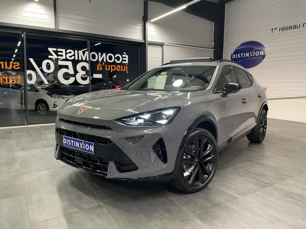 Vue 3/4 avant droit du CUPRA Formentor gris Graphene avec jantes noires et signature lumineuse Tri-LED allumée en intérieur showroom.