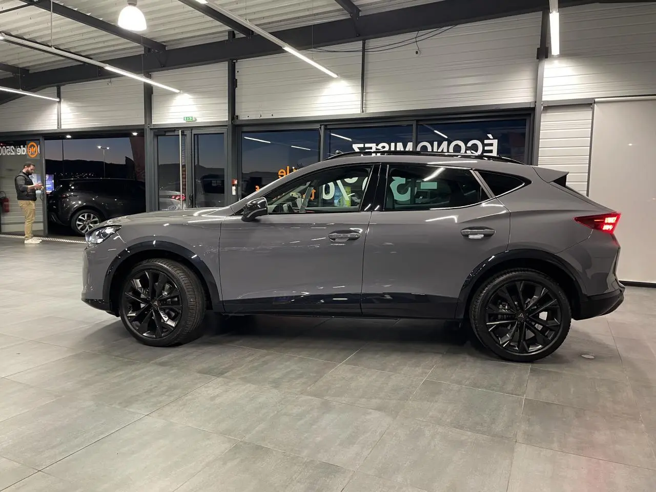 Vue de profil côté gauche d’un CUPRA Formentor gris Graphene avec jantes alliage noires en showroom.