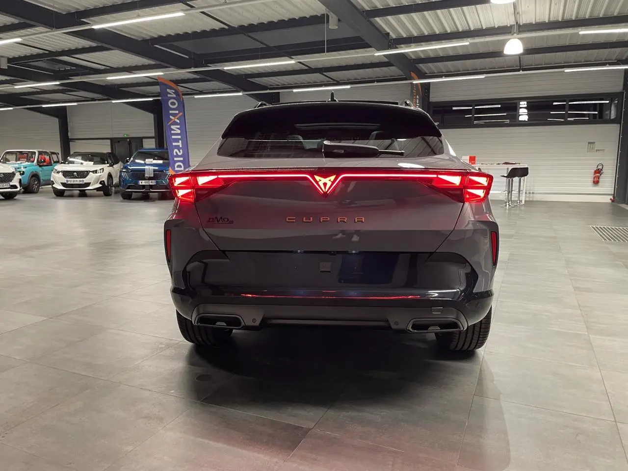 Vue arrière d'une CUPRA Formentor gris Graphene avec feux arrière Tri-LED allumés et double sortie d'échappement noire.