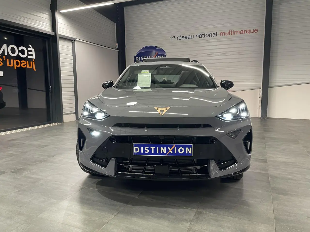 Vue frontale d'un CUPRA Formentor gris Graphene avec phares allumés et logo CUPRA cuivré visible sur le capot.