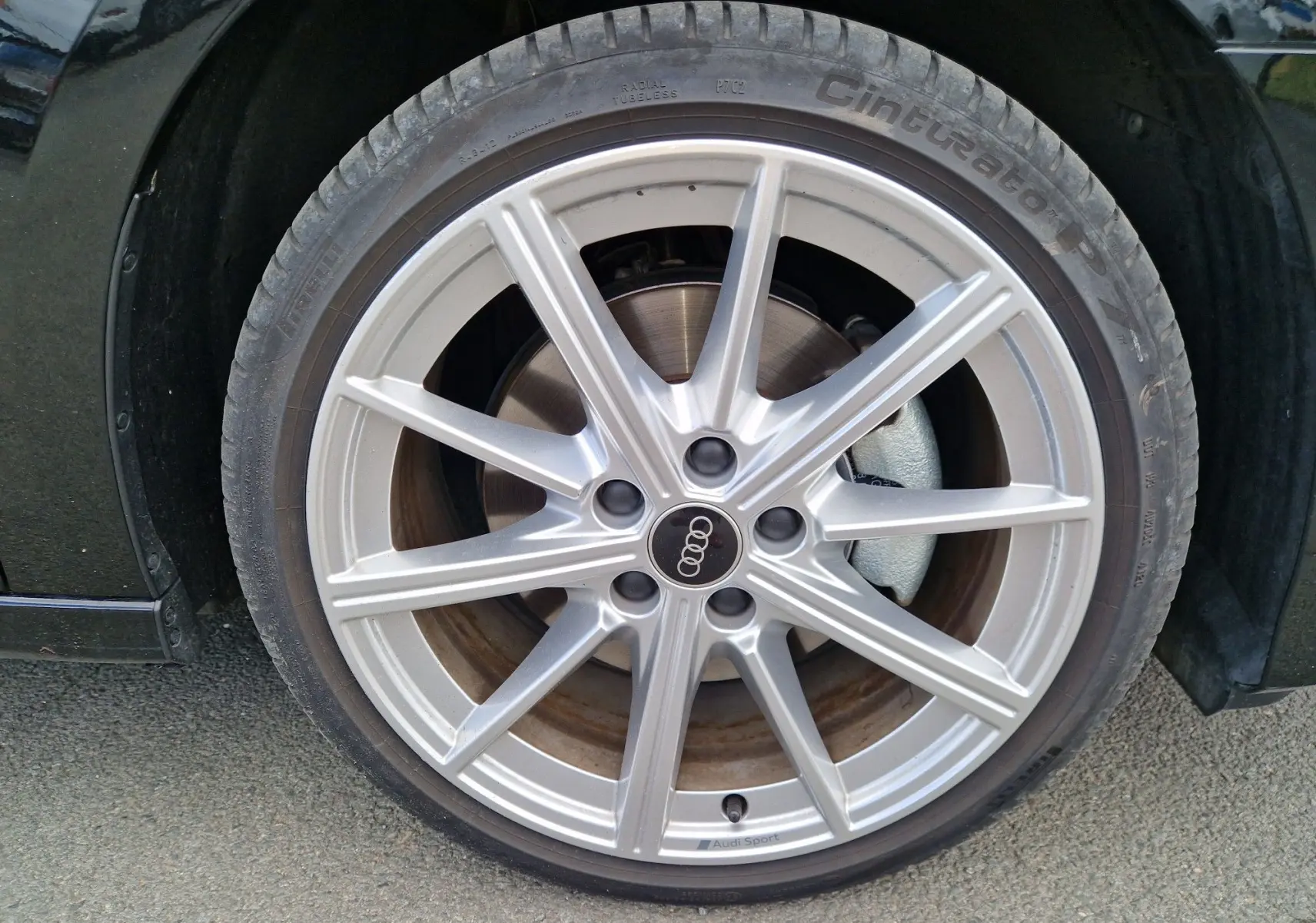 Gros plan sur la roue avant gauche d’une Audi A3 Sportback noire, jante alliage argentée Audi Sport visible.