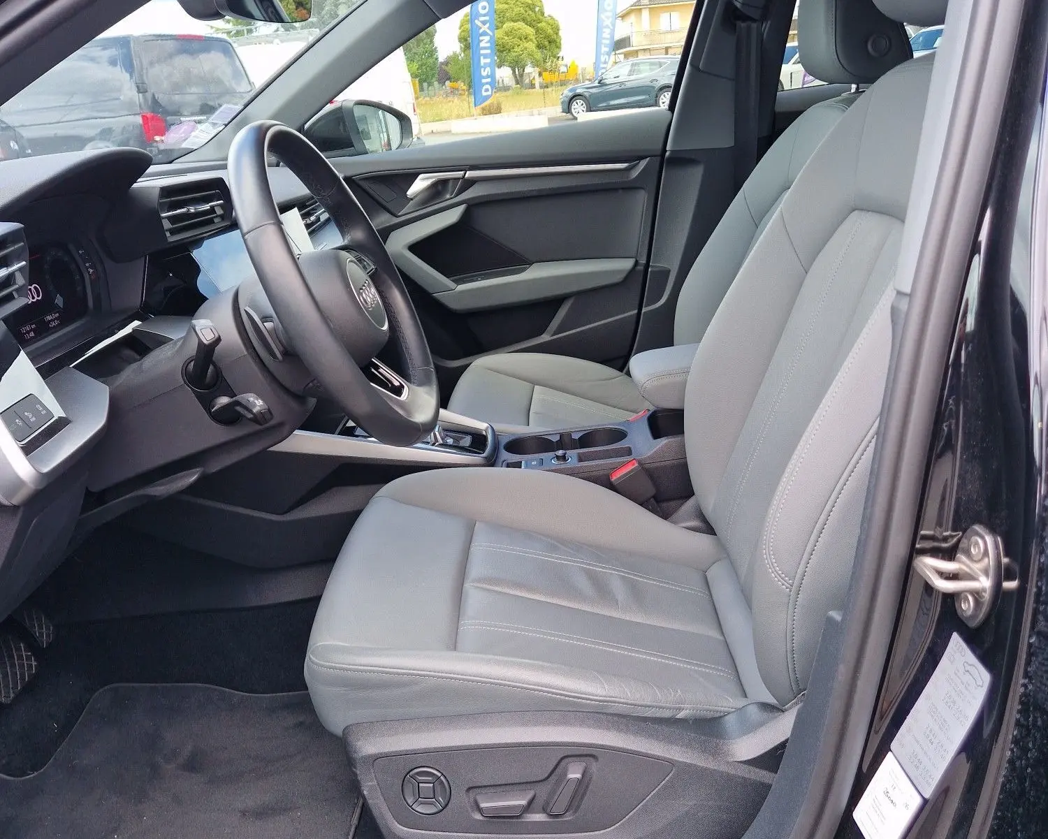 Vue intérieure côté conducteur de l'Audi A3 Sportback noire, mettant en valeur les sièges en cuir gris et le tableau de bord moderne.