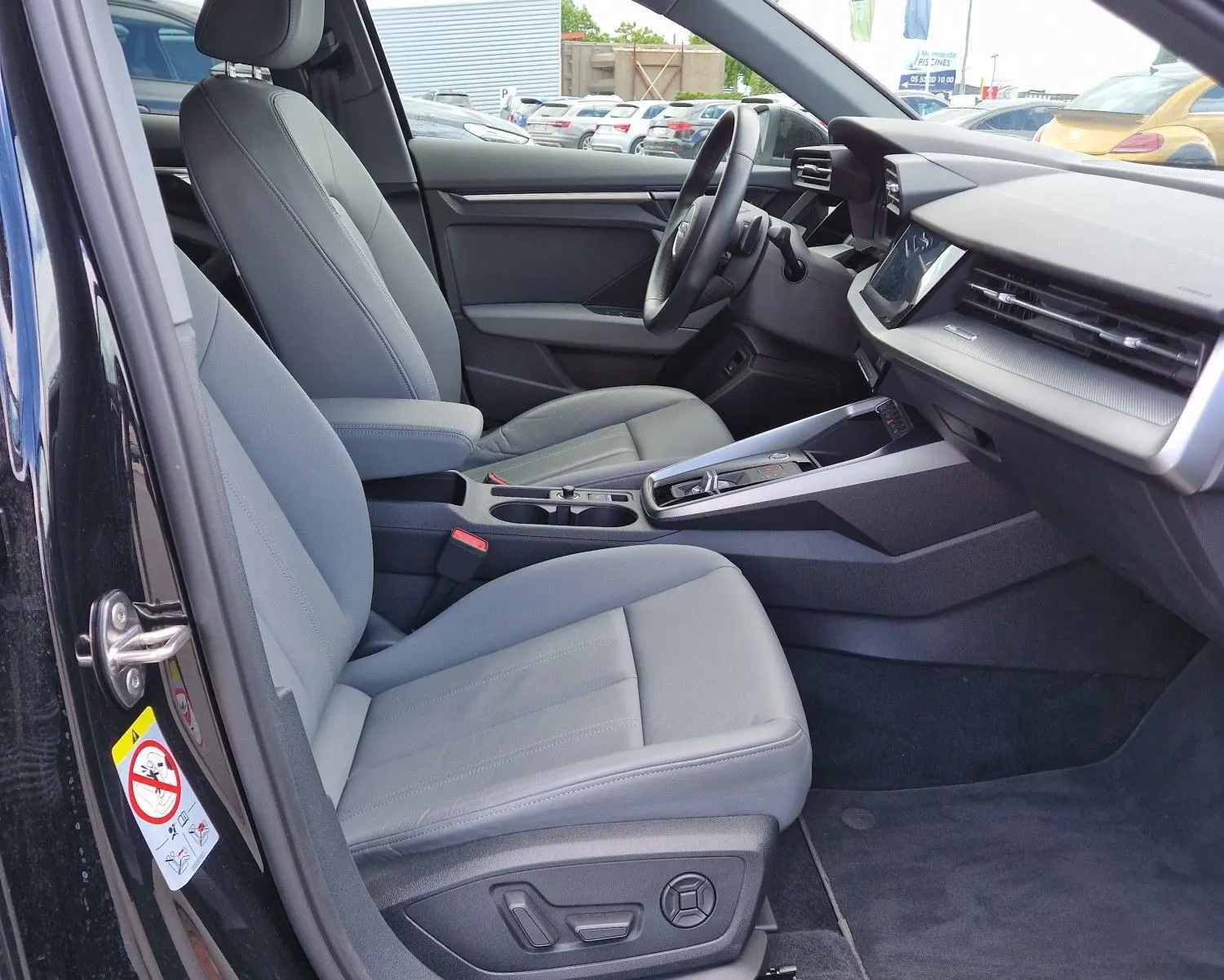 Vue intérieure côté conducteur de l'Audi A3 Sportback noire, mettant en valeur les sièges en cuir gris et le tableau de bord moderne.