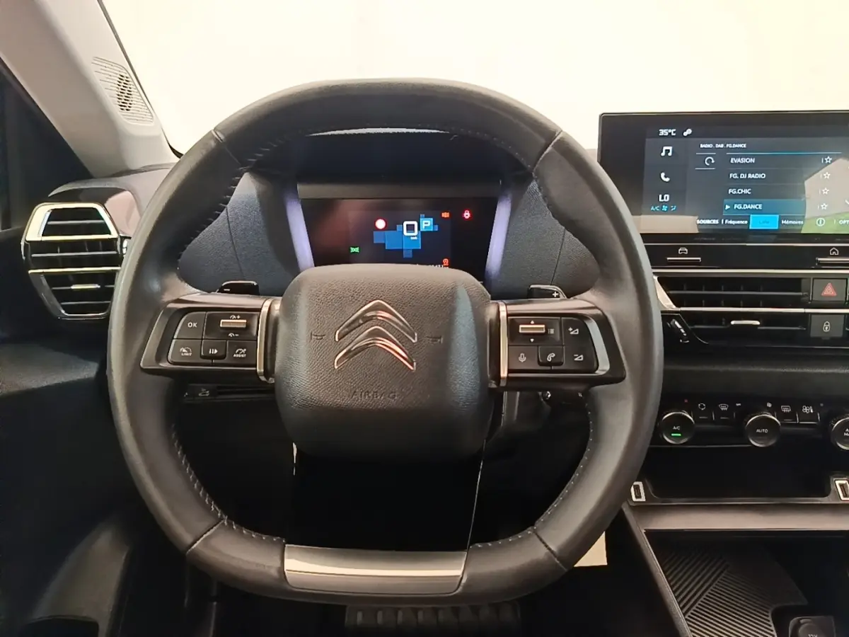 Vue intérieure centrée sur le volant cuir multifonctions noir du Citroën C4 X avec tableau de bord digital et écran tactile.