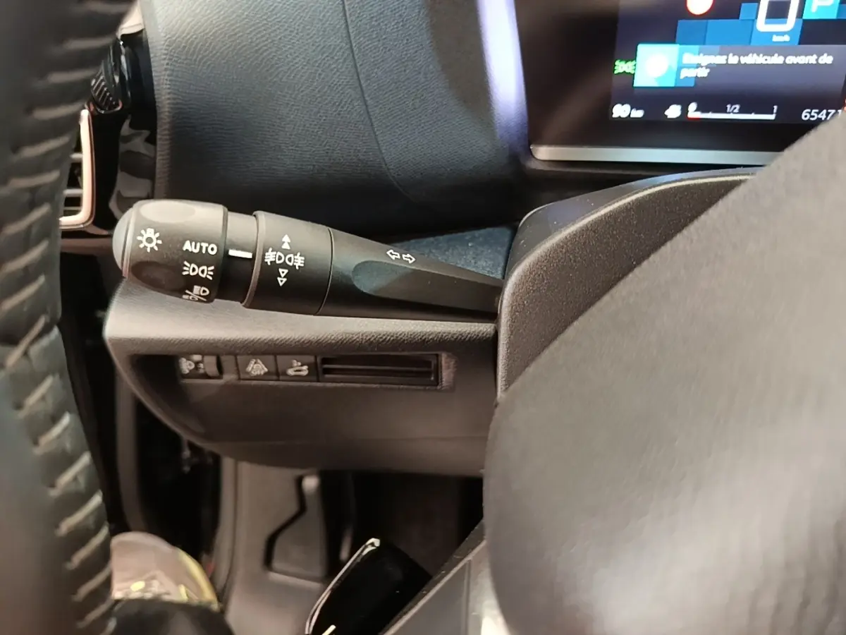 Gros plan sur la manette de commande des phares et clignotants à gauche du volant dans l’habitacle noir du Citroën C4 X.
