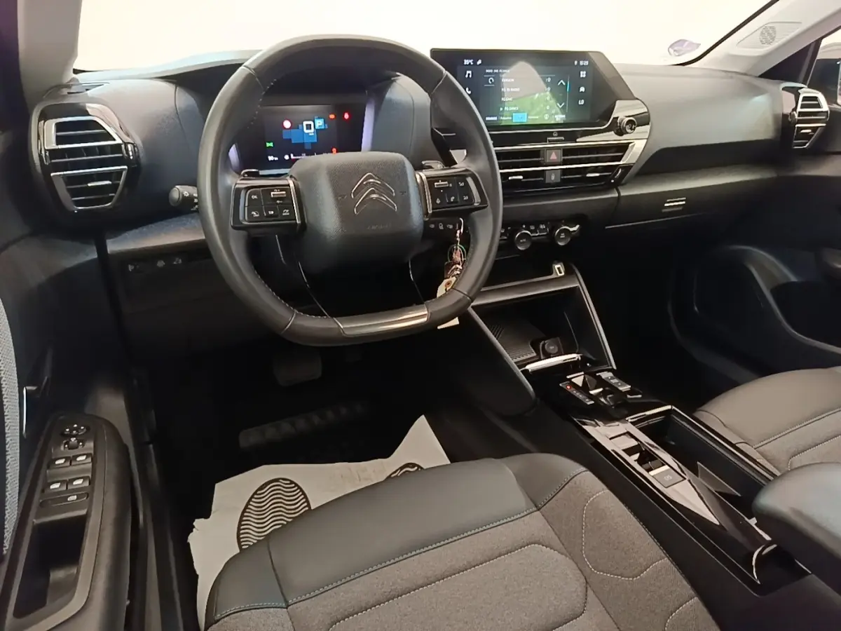 Intérieur de la Citroën C4 X noir, vue du poste de conduite avec volant cuir multifonctions et écran tactile central.