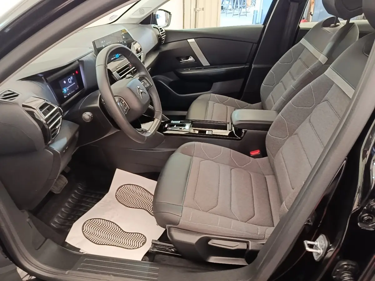 Intérieur avant droit d'une Citroën C4 X noire 2023, sièges tissu gris et volant cuir multifonctions.