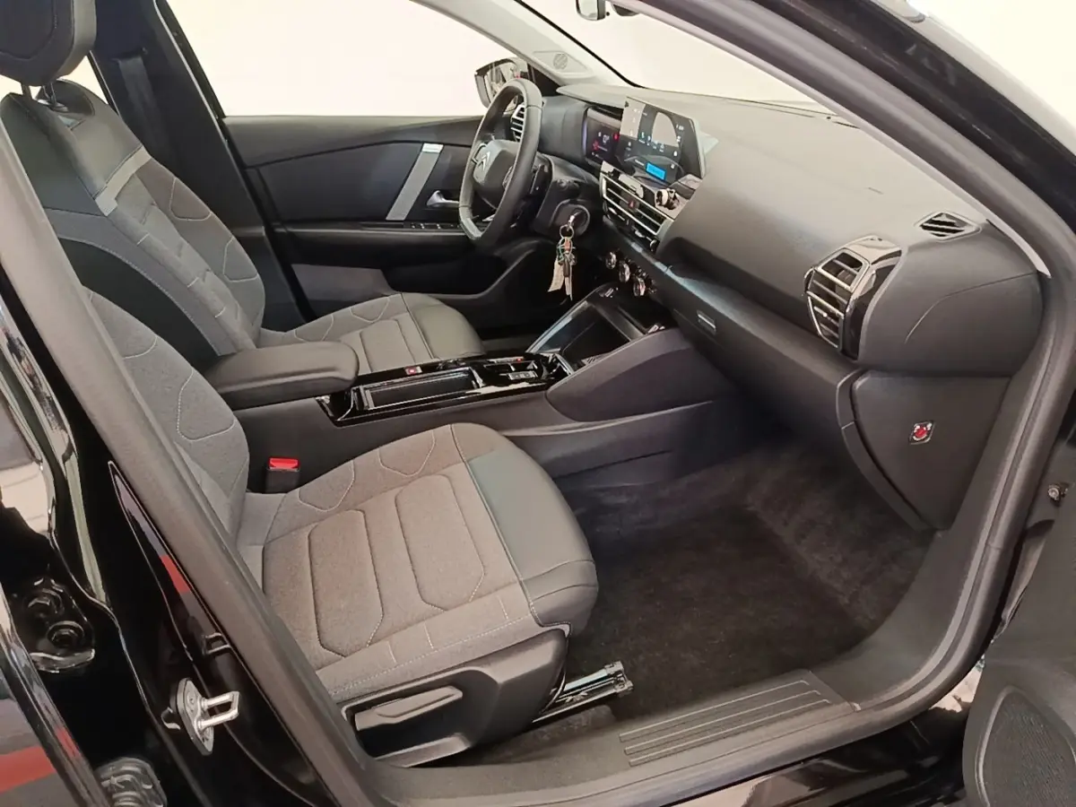 Vue intérieure côté conducteur de la Citroën C4 X noire 2023, sièges tissu gris et tableau de bord moderne.
