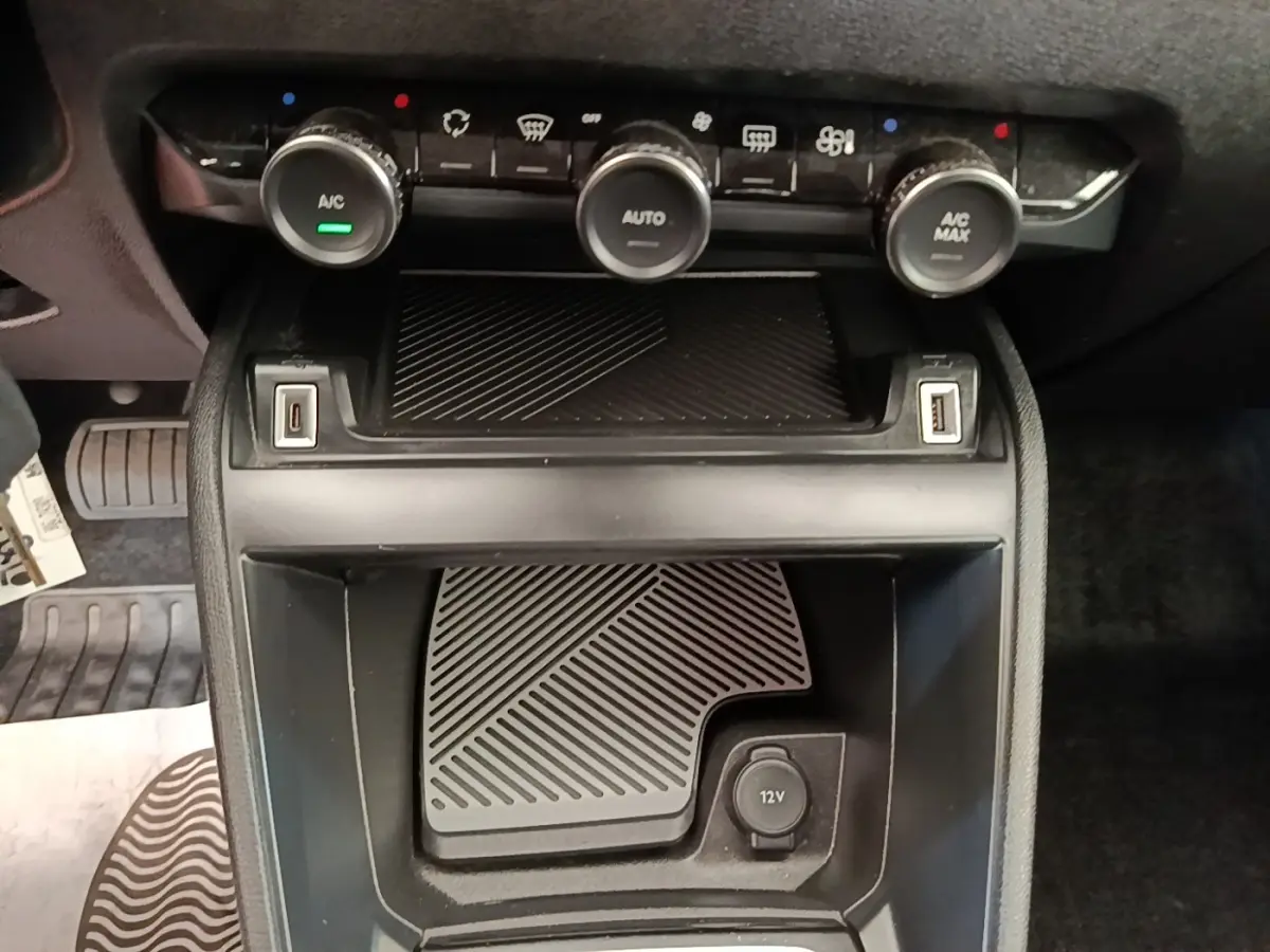 Vue rapprochée de la console centrale noire de la Citroën C4 X avec commandes climatisation et prises USB et 12V visibles.