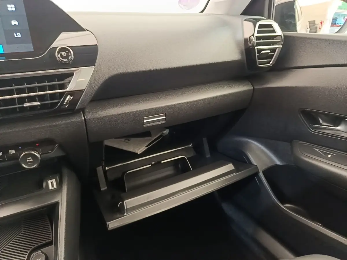 Intérieur noir de la Citroën C4 X 2023, vue côté passager avec boîte à gants ouverte et tableau de bord visible.