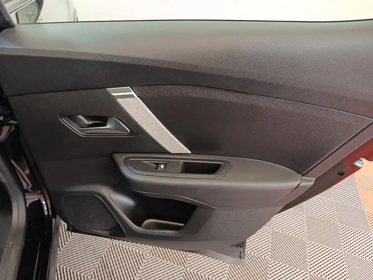 Vue intérieure de la porte arrière gauche noire d'une Citroën C4 X 2023, avec poignée et commande de vitre.