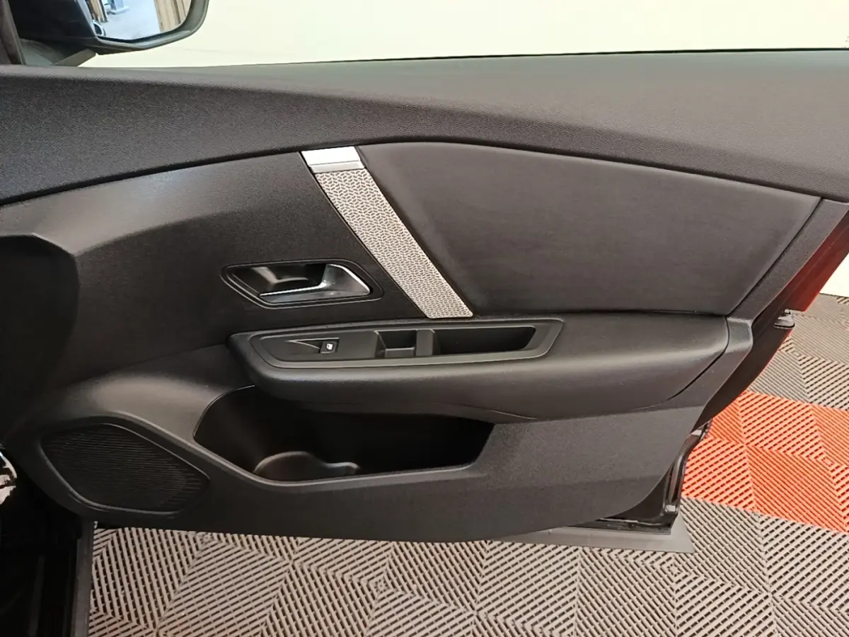 Vue intérieure du panneau de porte avant gauche noir de la Citroën C4 X 2023 avec poignée et commande de vitre.
