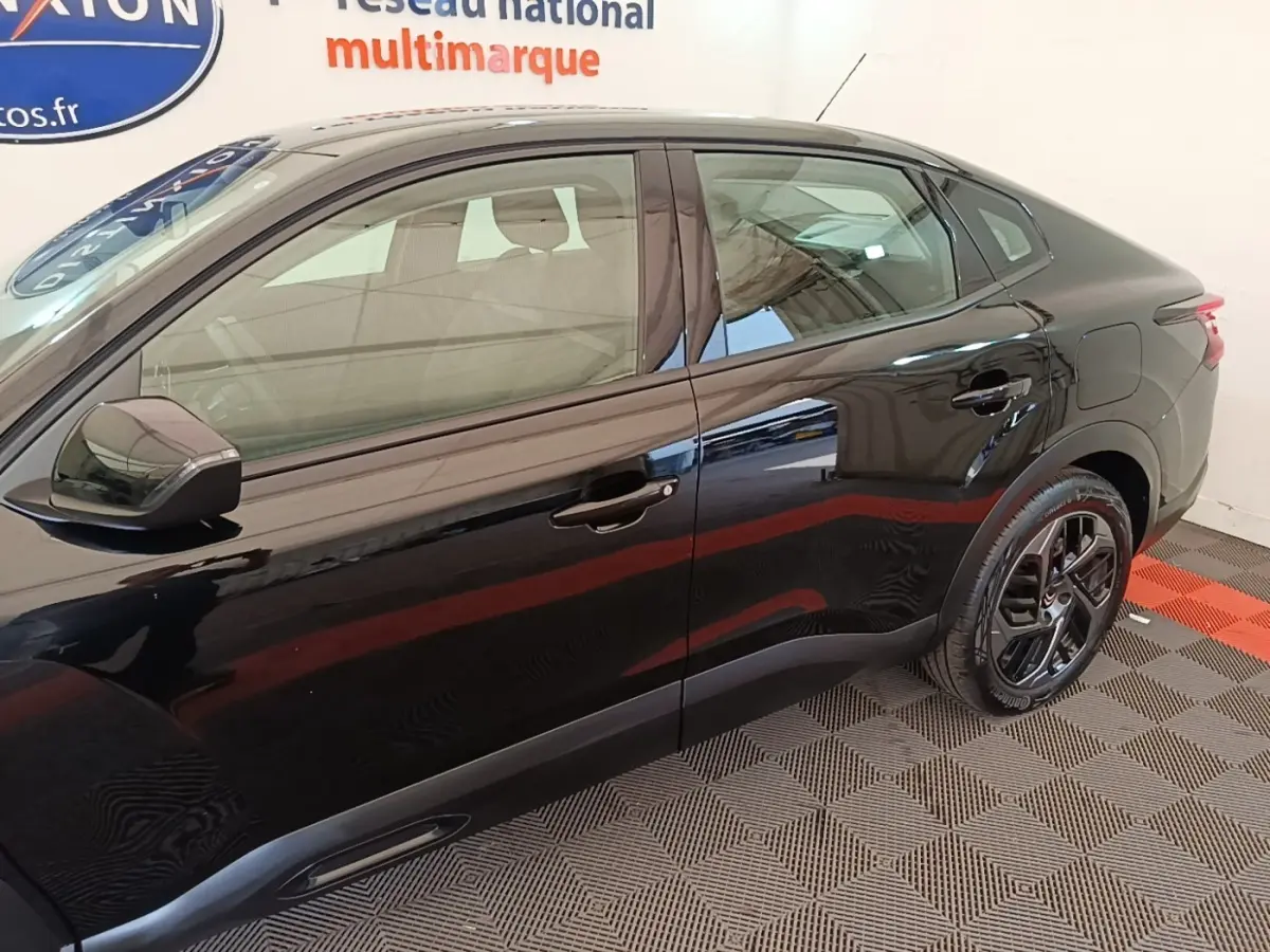 Vue latérale droite d'une Citroën C4 X noire 2023 avec jantes noires et lignes fluides sur fond intérieur.