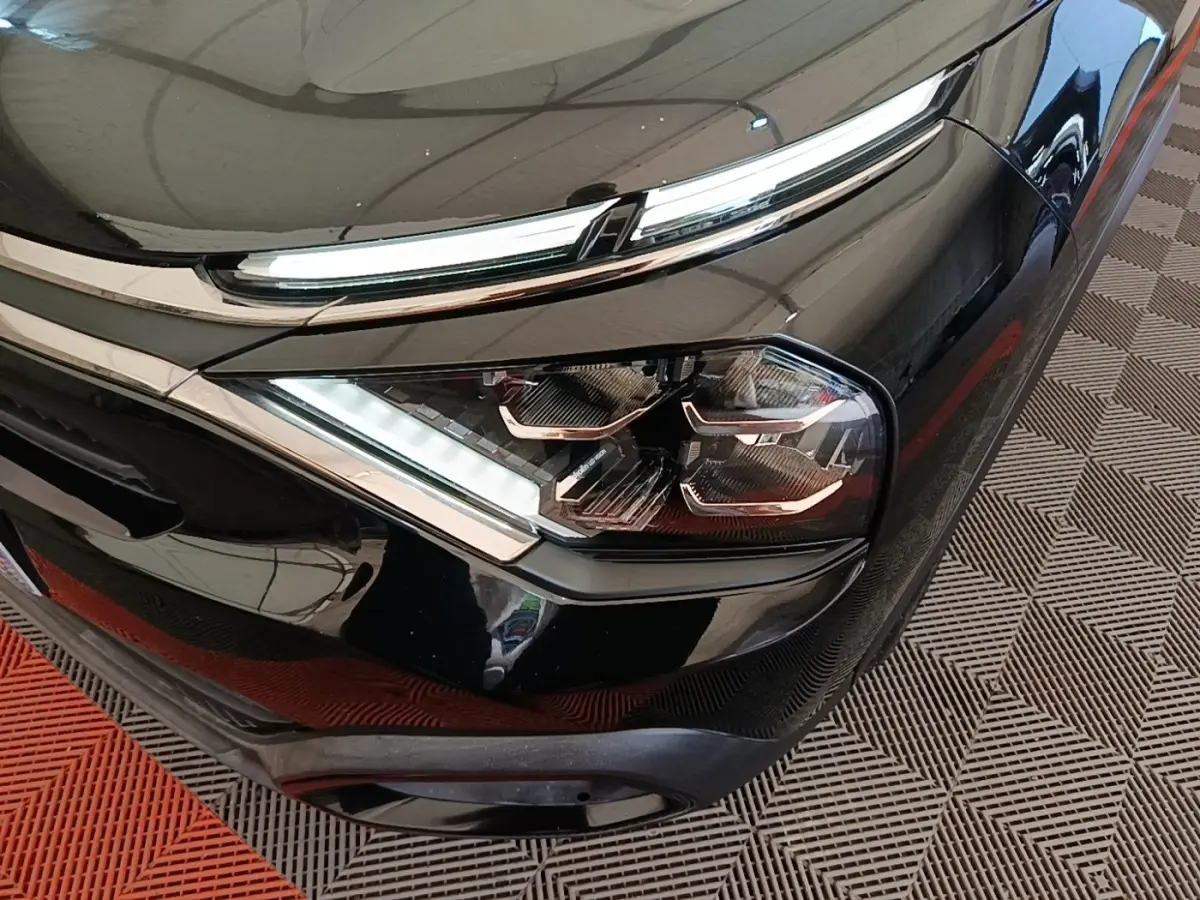 Gros plan sur le phare avant droit noir brillant du Citroën C4 X 2023 avec détails LED et calandre chromée.