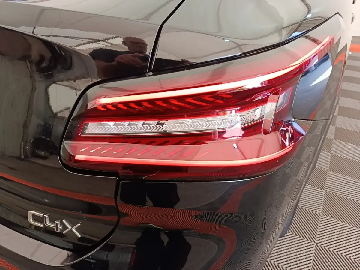 Gros plan sur le feu arrière droit rouge d’une Citroën C4 X noire, avec logo C4 X visible sur le coffre.
