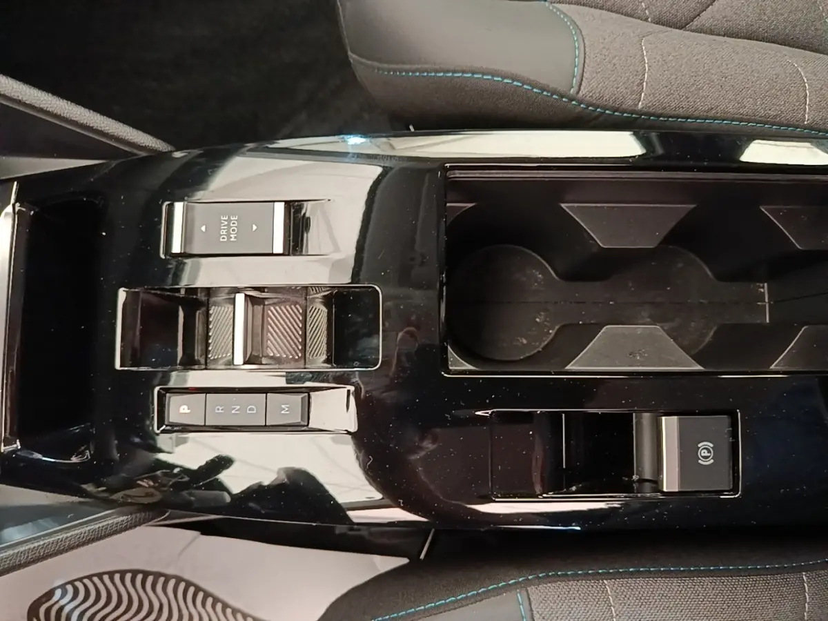 Vue rapprochée de la console centrale noire brillante de la Citroën C4 X avec commandes de boîte auto et porte-gobelets.