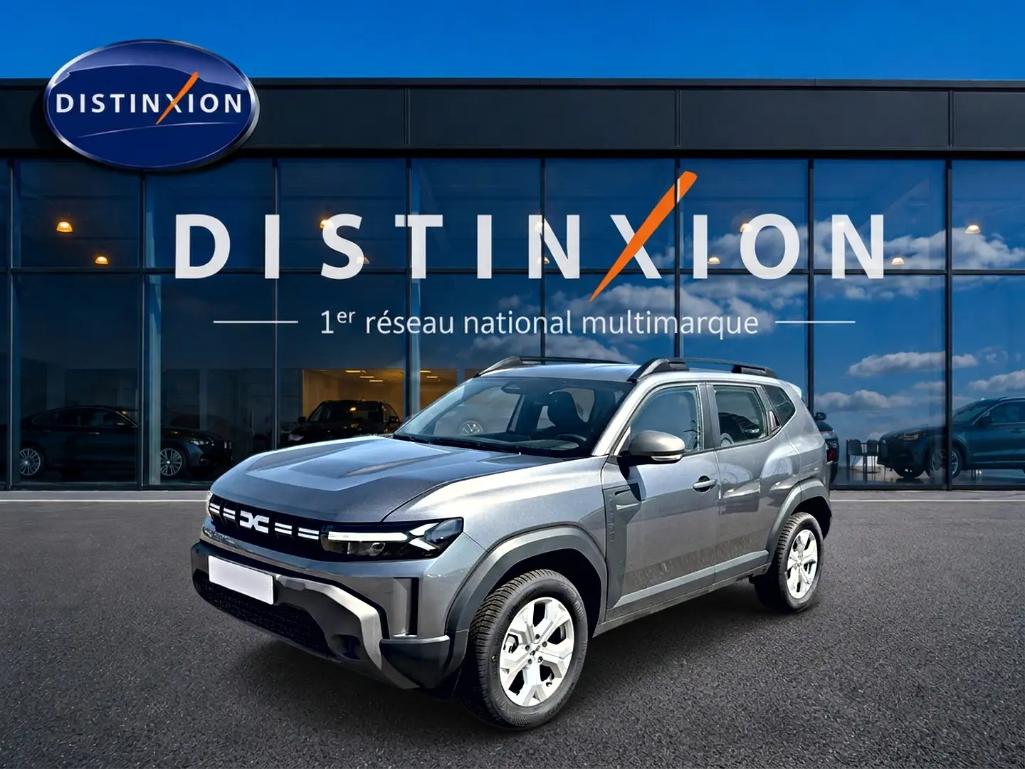 Dacia Duster 1.2 hybrid-g 150 gris schiste en 3/4 avant droit, avec barres de toit et jantes alu visibles.