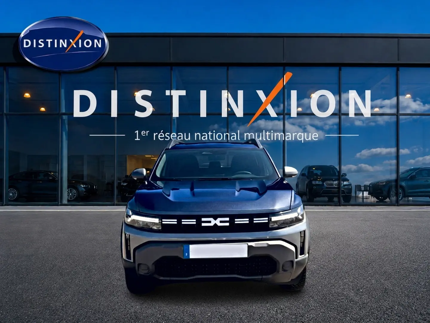 Vue avant d'un Dacia Duster gris schiste 2026 avec calandre lumineuse, devant une vitrine Distinxion.
