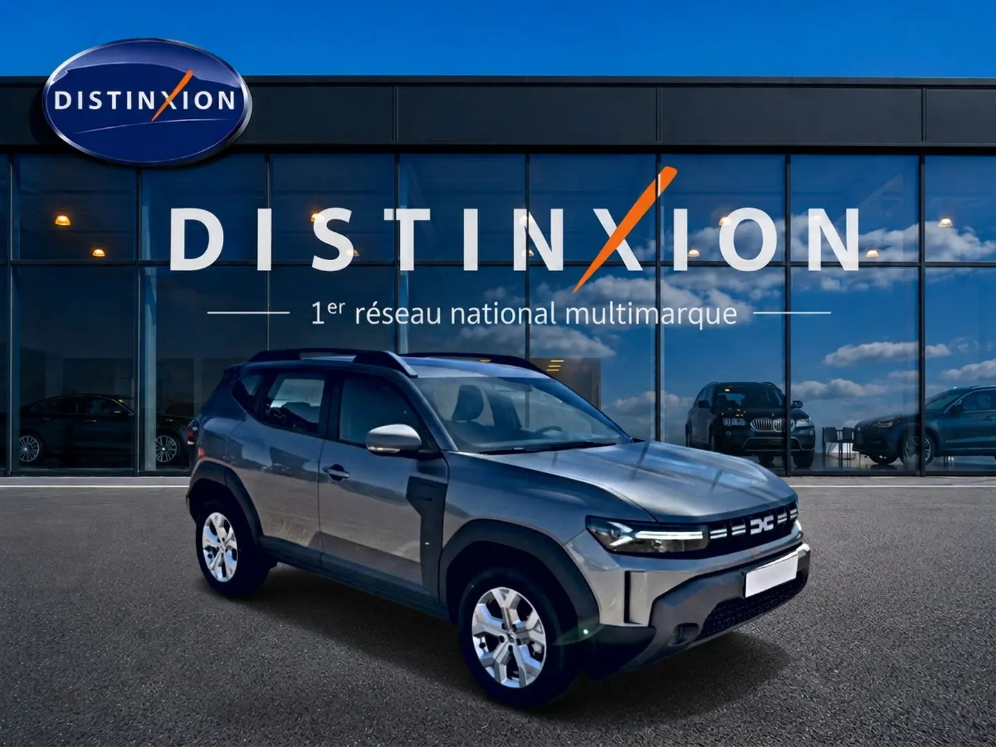 Dacia Duster gris schiste en 3/4 avant droit, avec jantes alu et rétroviseurs argentés devant showroom Distinxion.