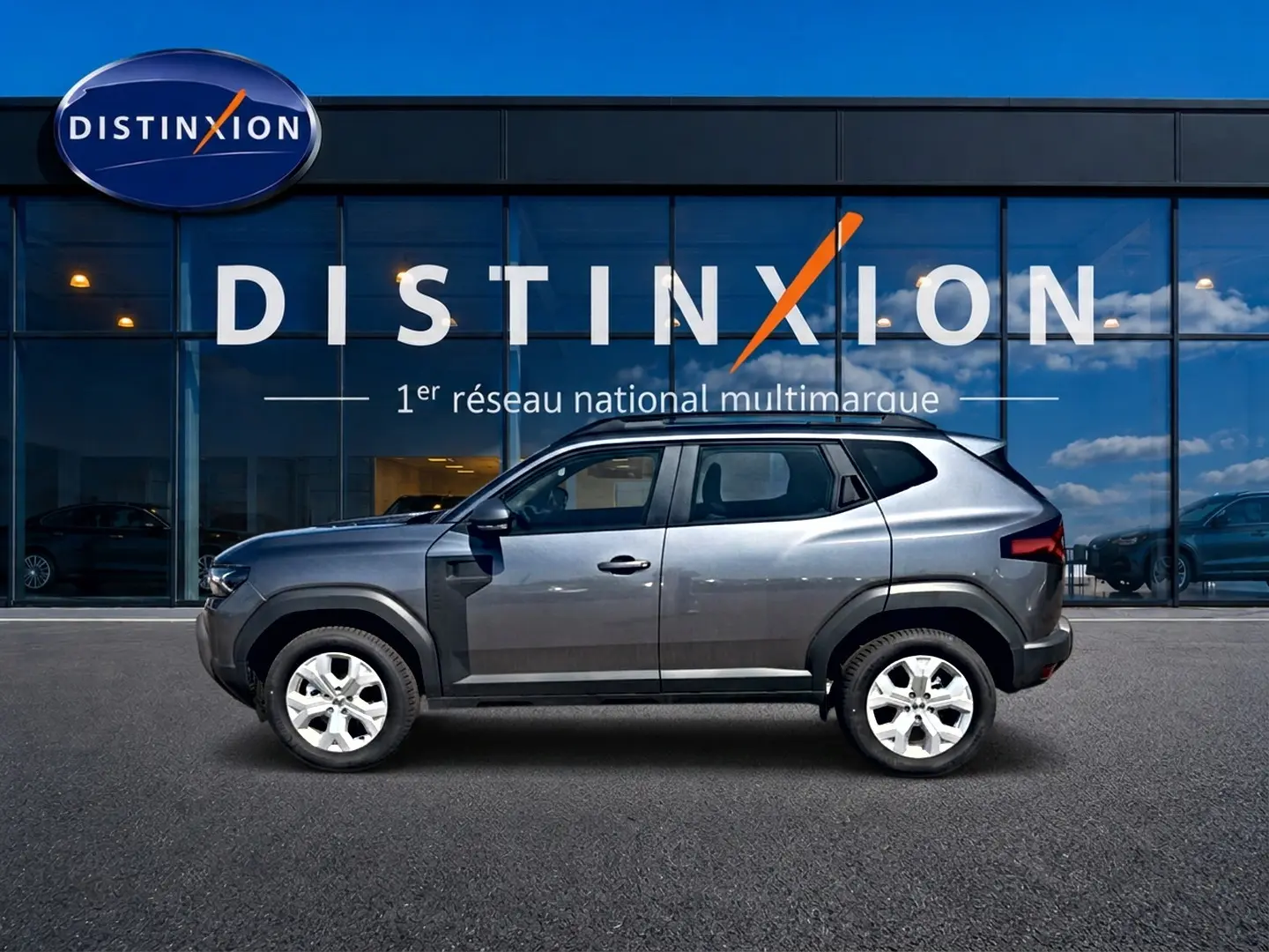 Profil droit du Dacia Duster gris schiste 2026 devant une vitrine avec logo Distinxion.