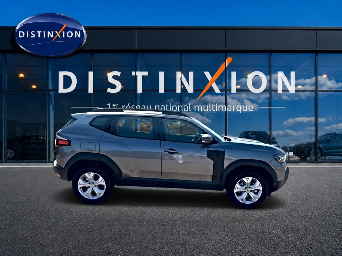 Profil droit du Dacia Duster gris schiste 2026 devant une vitrine avec logo Distinxion.