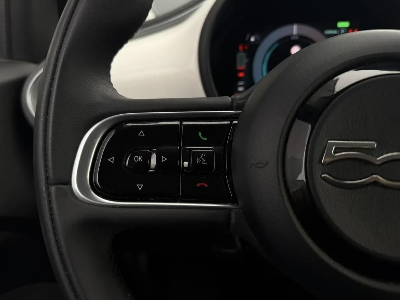 Gros plan sur la partie gauche du volant noir de la FIAT 500 électrique blanche avec commandes intégrées.