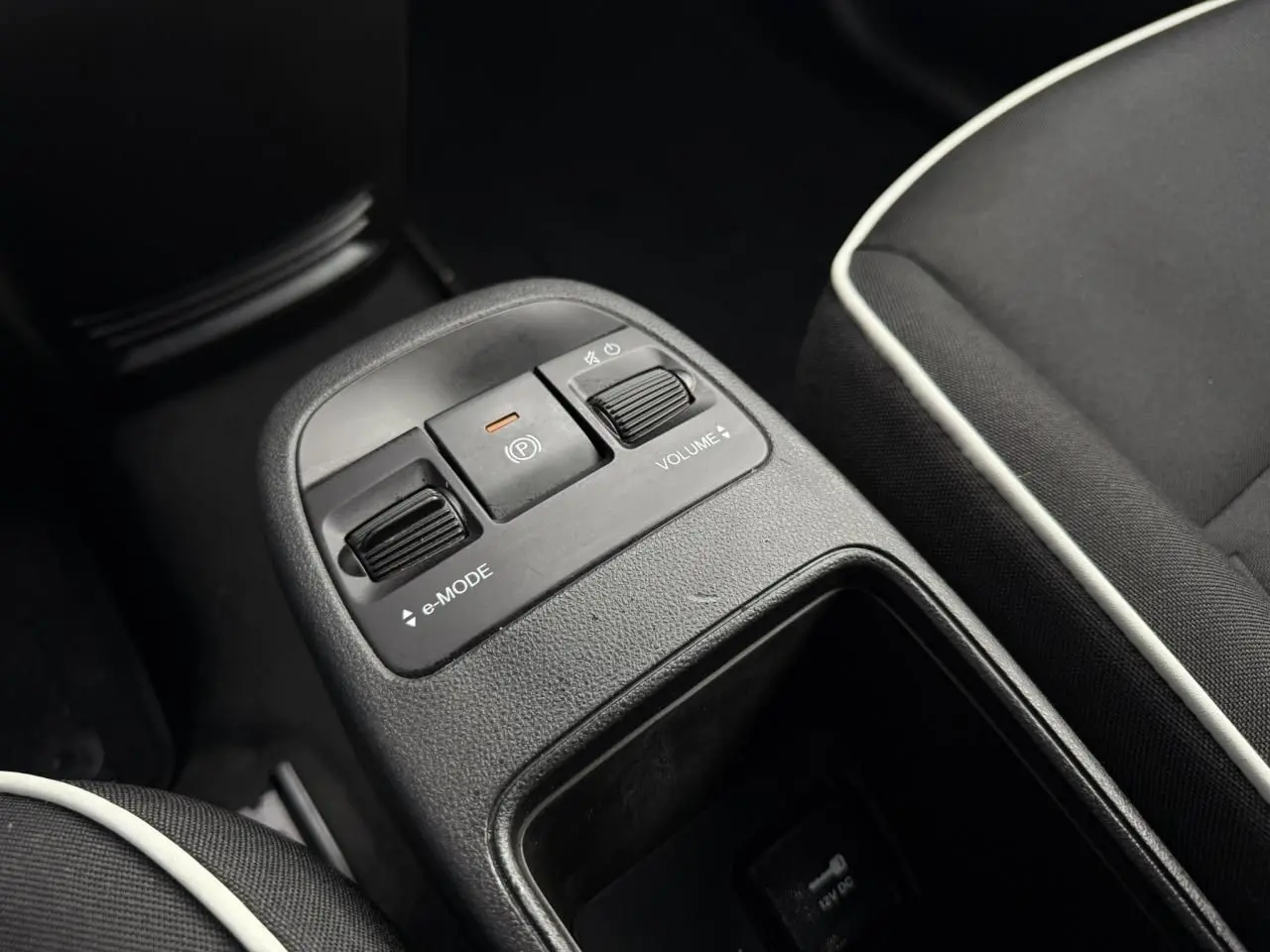 Gros plan sur la console centrale noire de la Fiat 500 électrique 2024, avec commandes e-mode et volume, sièges tissu noir.