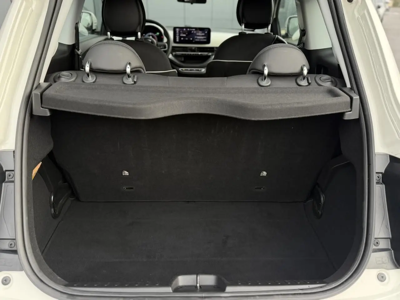 Coffre ouvert d'une FIAT 500 électrique blanche, vue arrière montrant l'intérieur et l'écran tactile du tableau de bord.