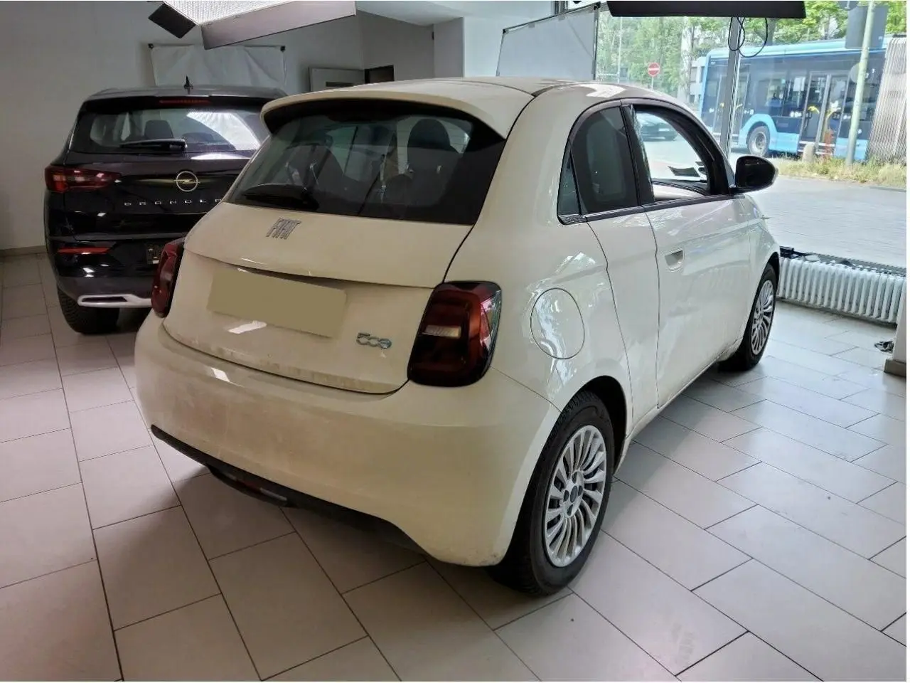 Vue 3/4 arrière droite d'une Fiat 500 électrique blanche, avec feux arrière foncés et jantes multibranches en showroom.