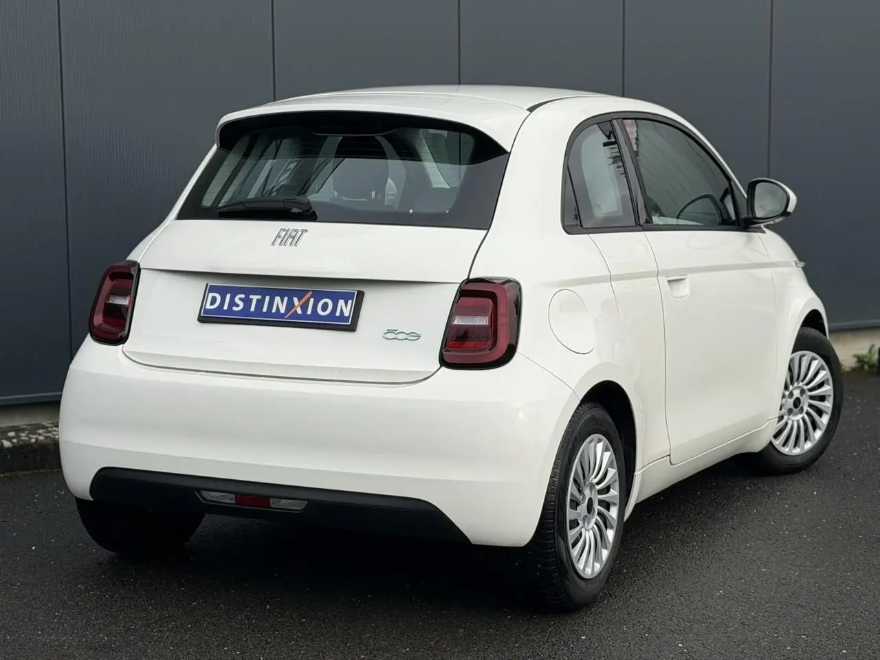 Vue 3/4 arrière droite d'une Fiat 500 électrique blanche 2024 avec feux arrière foncés et jantes multibranches.