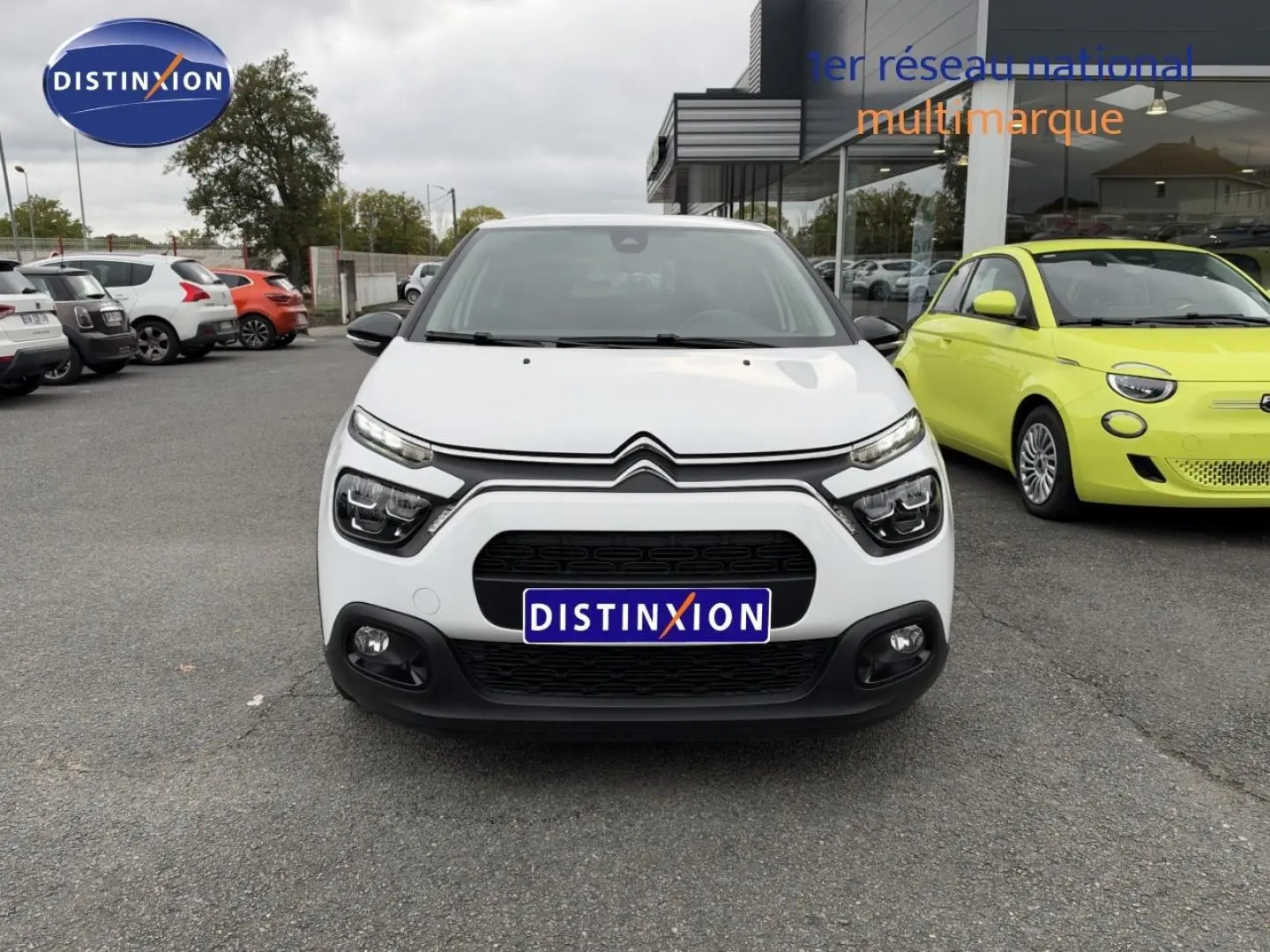 Vue avant d'une Citroën C3 blanche Banquise avec calandre noire et phares LED, stationnée devant un showroom.