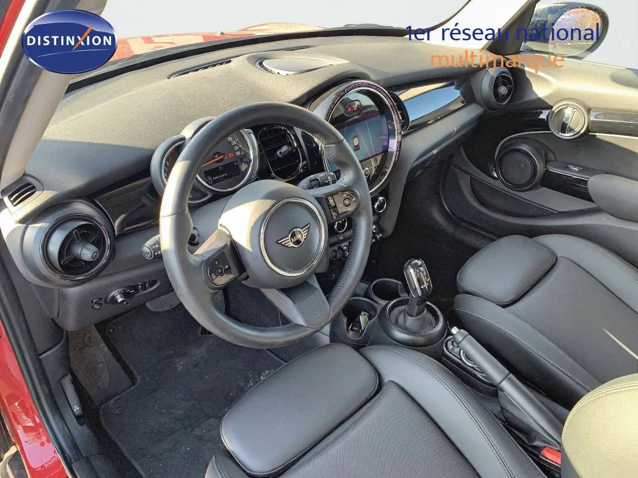 Intérieur avant droit d'une MINI rouge chili 2023 avec tableau de bord moderne et sièges cuir noir.