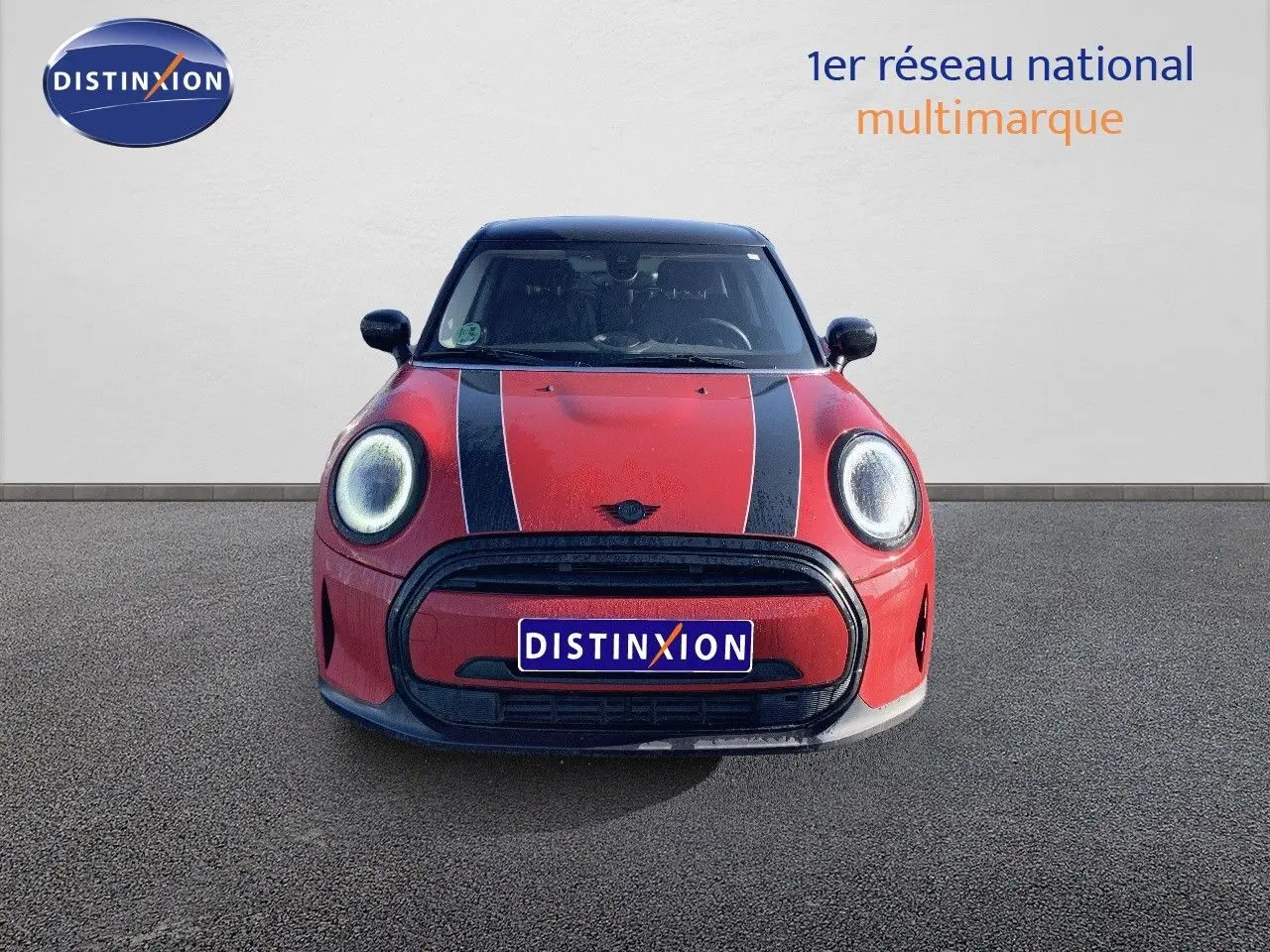 Vue frontale d'une MINI 1.5 136CH STEPTRONIC rouge chili avec bandes noires sur le capot et phares LED ronds.