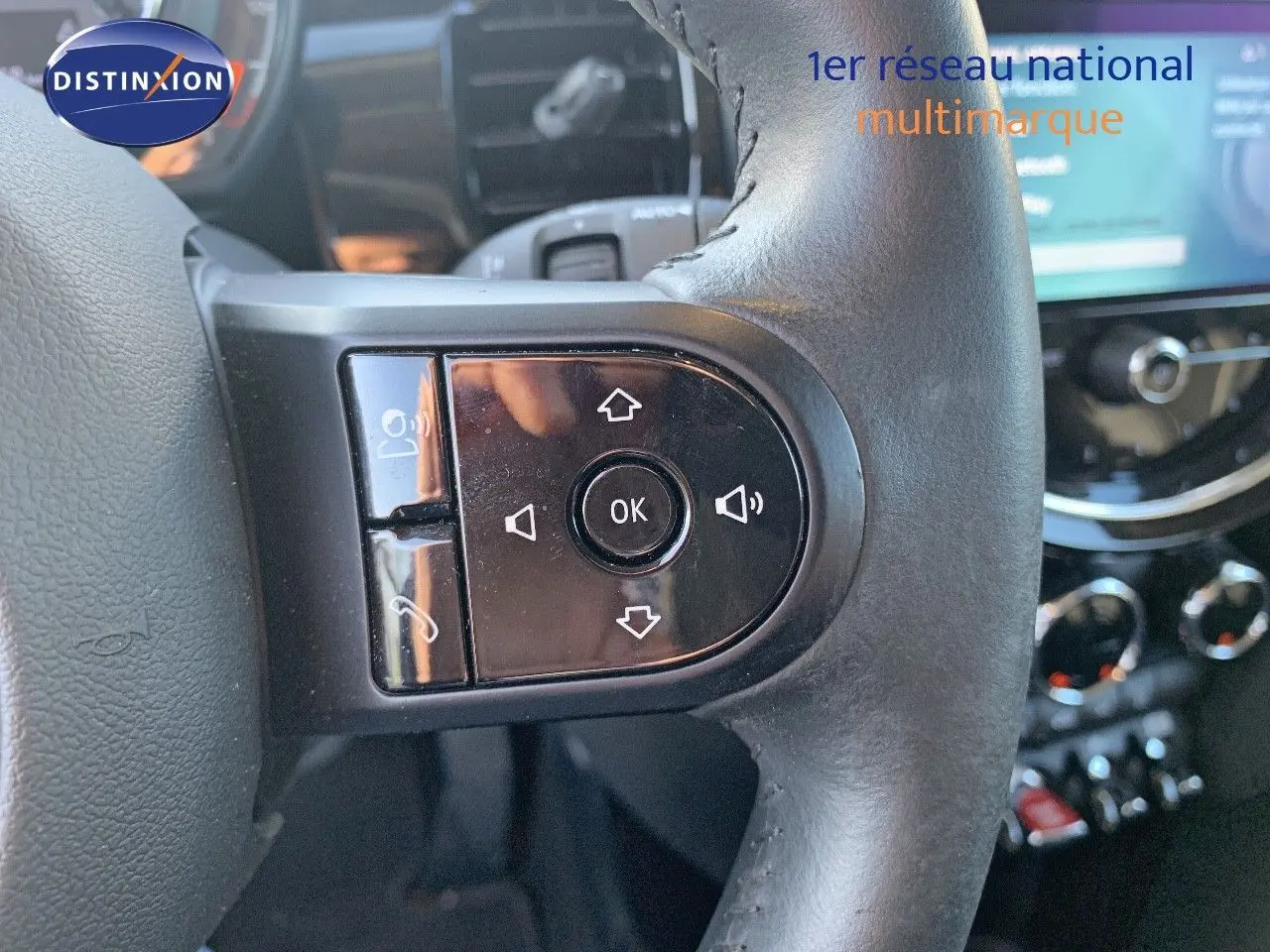 Gros plan sur les commandes noires du volant d'une MINI 1.5 136CH rouge chili, avec tableau de bord flou en arrière-plan.