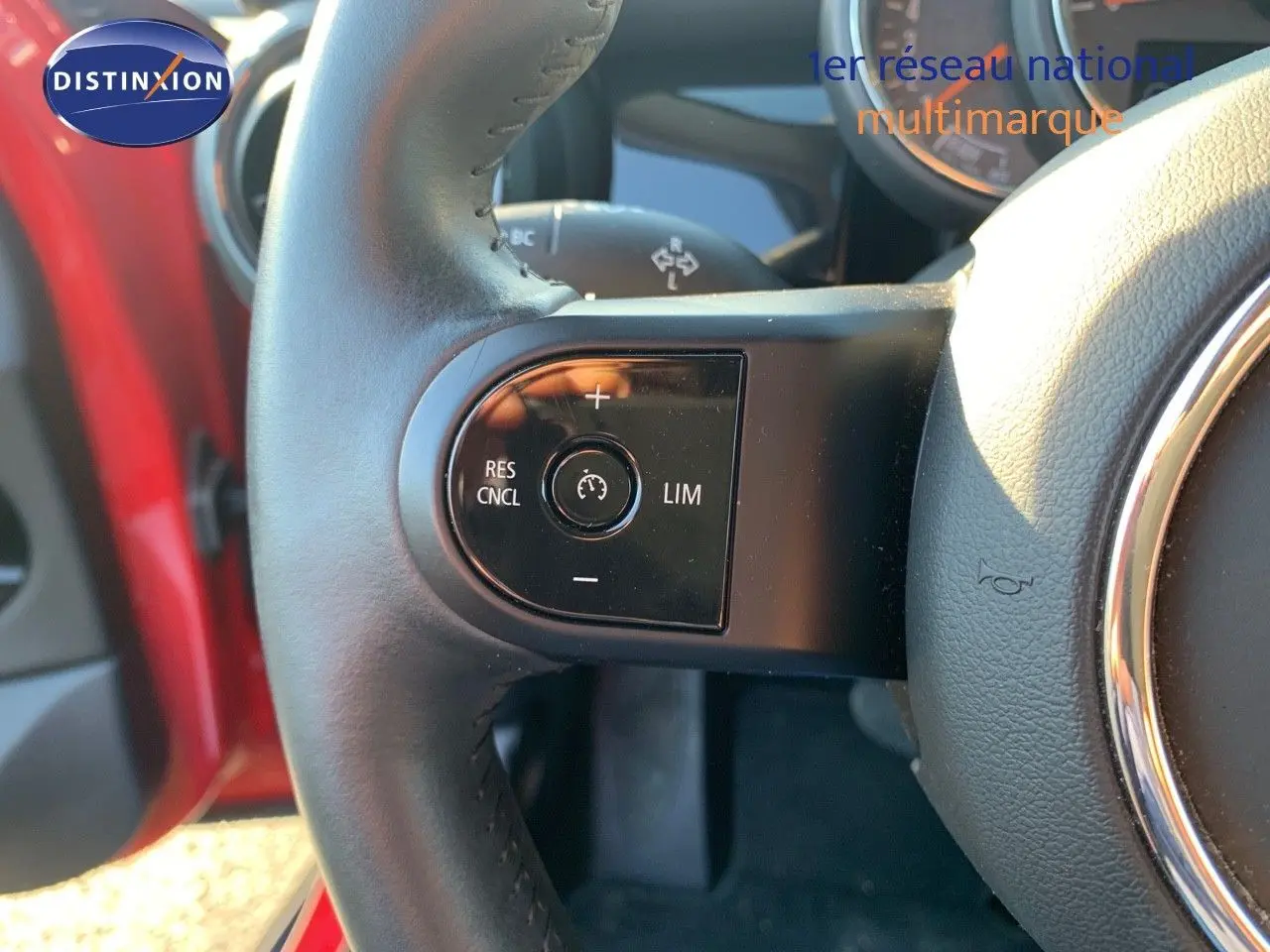 Gros plan sur le volant de la MINI 2023 rouge chili, montrant les commandes de régulateur de vitesse à gauche.