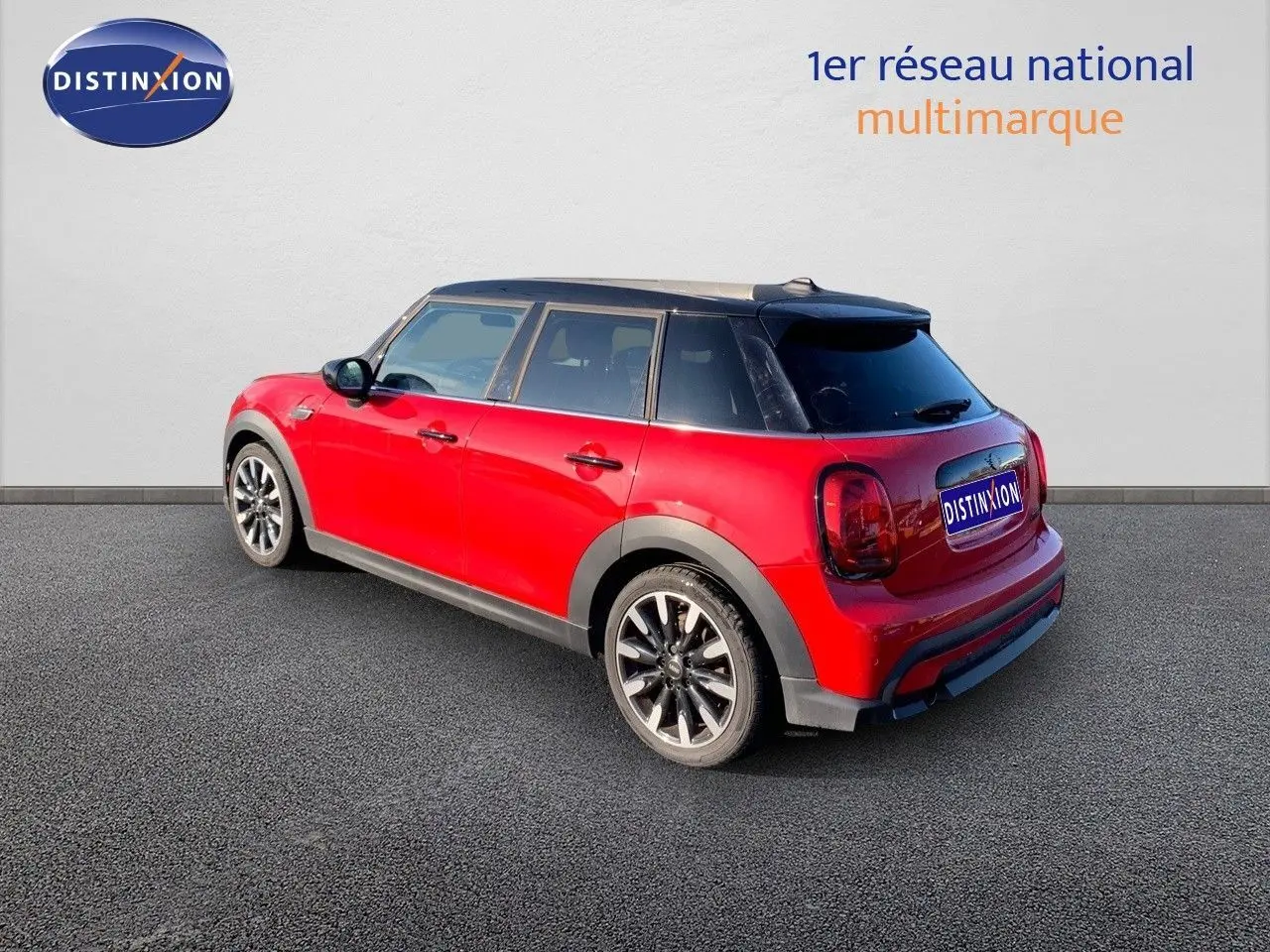 Vue 3/4 arrière droite d'une MINI 1.5 136CH rouge chili à toit noir, avec jantes noires et cinq portes visibles.