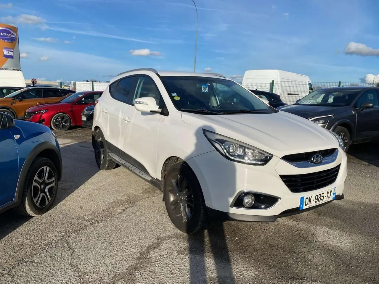 Hyundai ix35 blanc vu en 3/4 avant droit sur un parking, avec jantes foncées et projecteurs allumés.