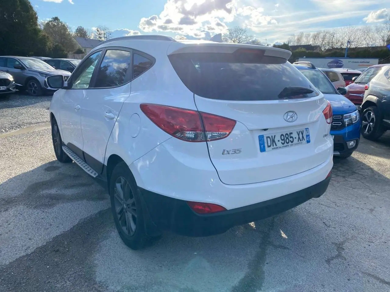 Vue 3/4 arrière droite d'un Hyundai ix35 blanc avec vitres teintées et jantes foncées sur un parking.