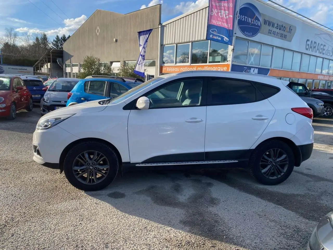 Vue de profil côté gauche d'un Hyundai ix35 blanc stationné devant un garage, avec jantes alliage foncé.