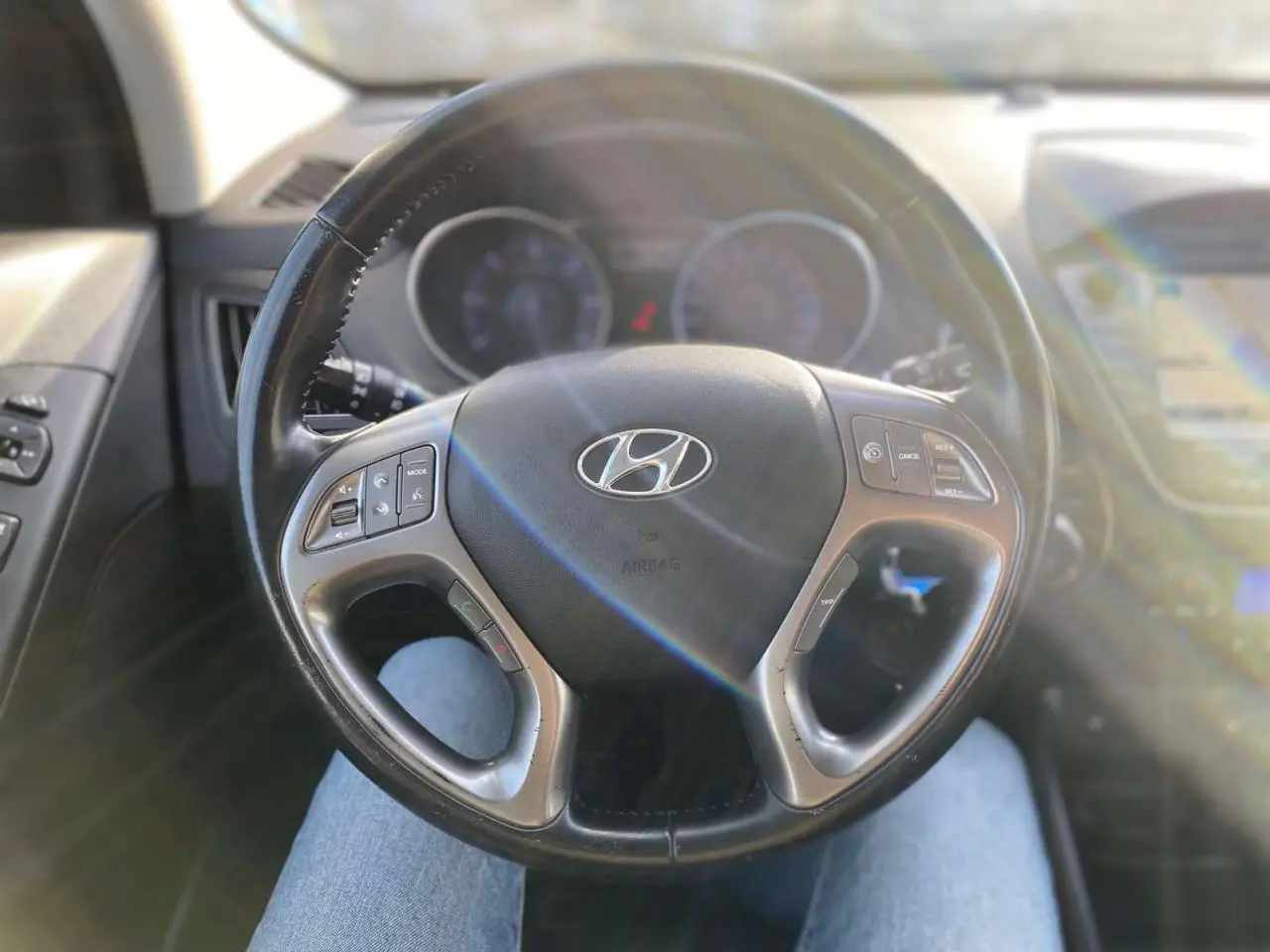 Volant cuir du Hyundai ix35 2014 vu de face, avec commandes intégrées et tableau de bord flou en arrière-plan.