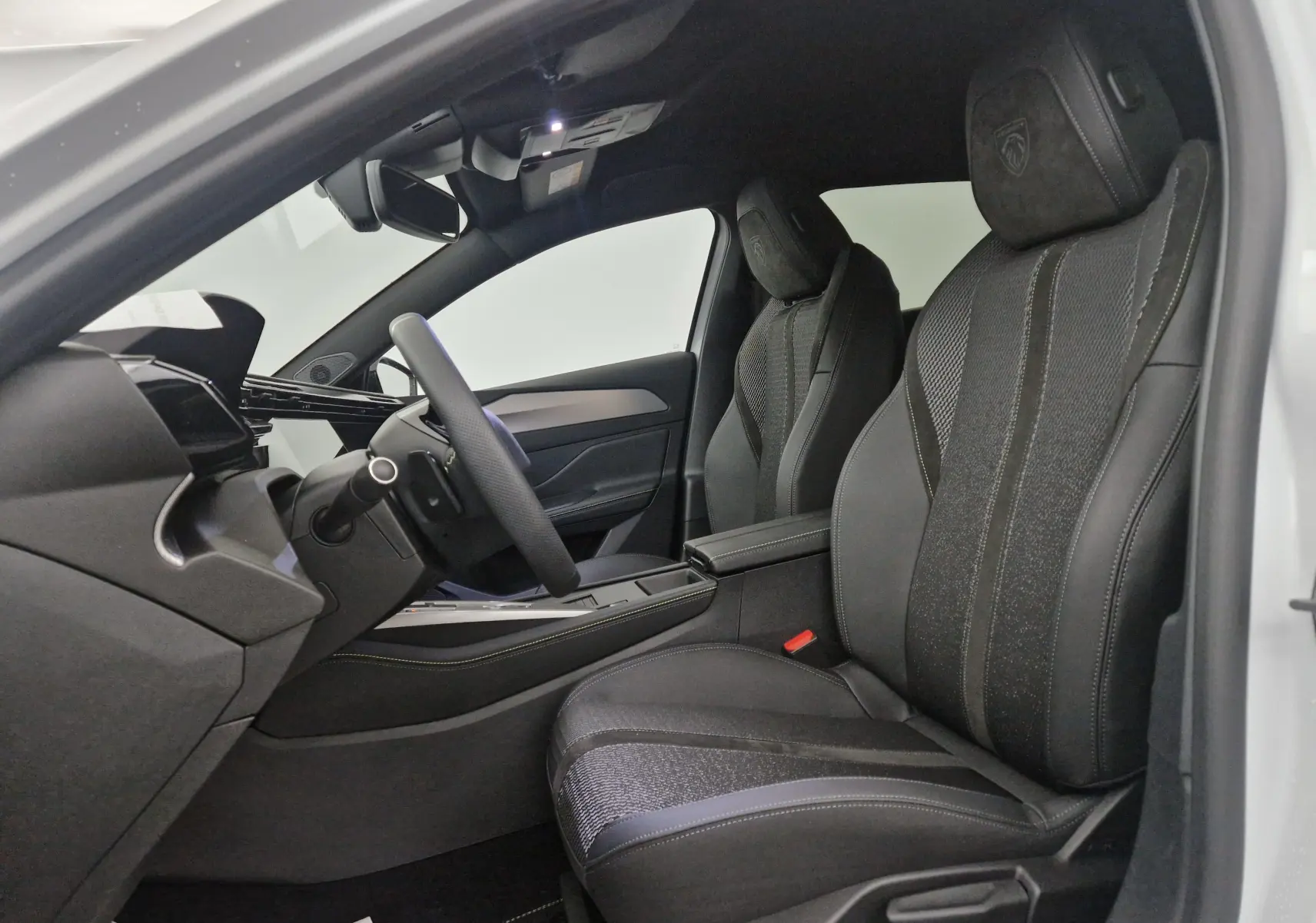 Vue intérieure côté conducteur de la Peugeot 308 2025 blanc Okenite, sièges sport en cuir et tissu avec logo Peugeot brodé.