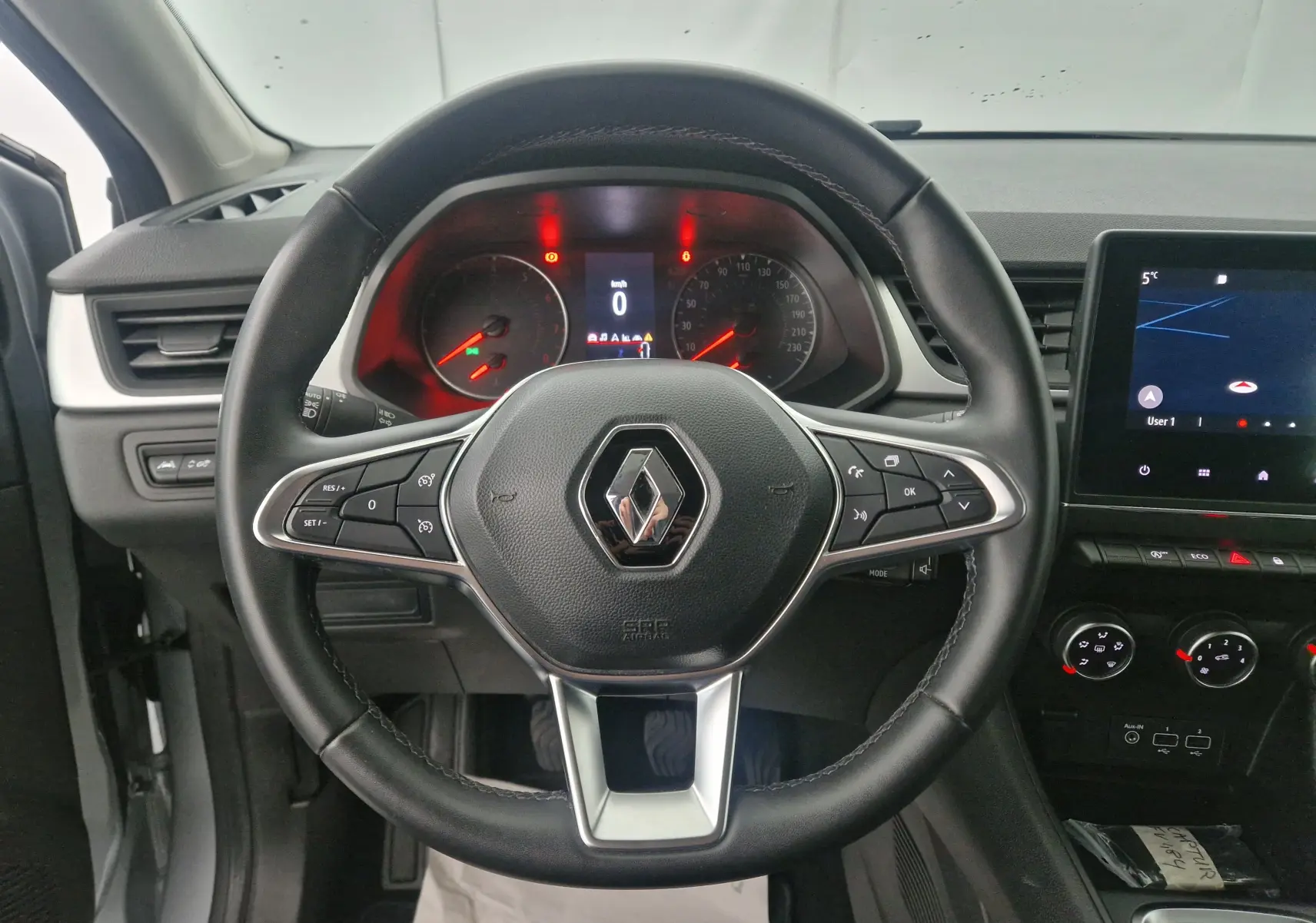 Vue intérieure centrée sur le volant du Renault Captur gris Highland, avec tableau de bord et écran tactile GPS visibles.