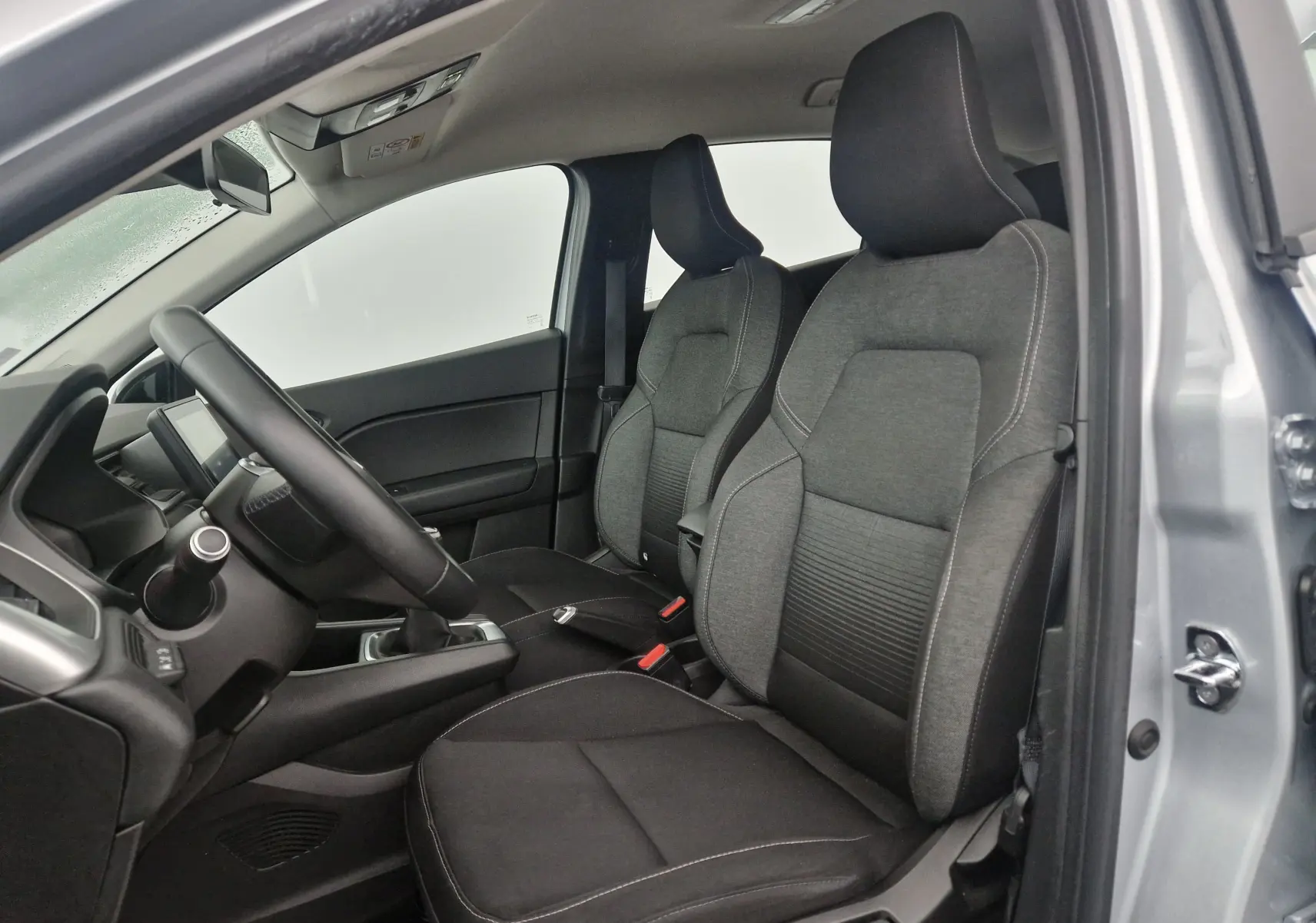 Vue intérieure côté conducteur du Renault Captur gris Highland 2020, montrant les sièges avant en tissu et le volant.