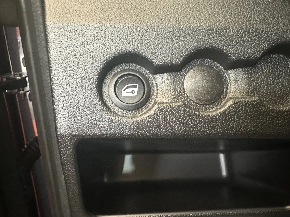 Gros plan sur le bouton d'ouverture du coffre dans l'habitacle noir de l'AIXAM AMBITION 0.5 CITY SPORT rouge.