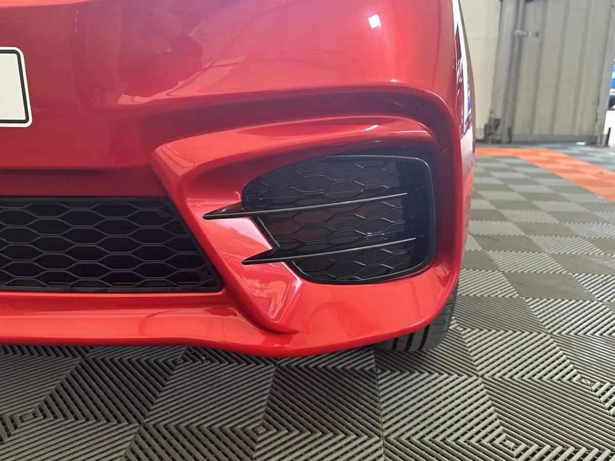 Gros plan sur la partie avant droite rouge de l'AIXAM AMBITION 0.5 CITY SPORT avec grille noire et détails sportifs.